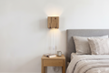 Bedroom with wooden nightstand, wall lamp, and bed with gray headboard and pillows.